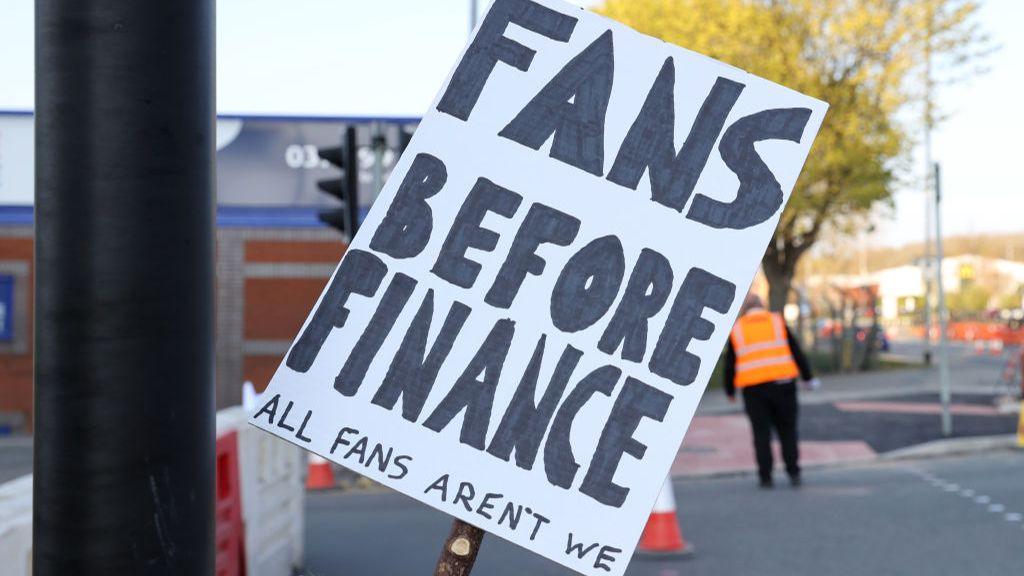 A fan sign reading "Fans before finance. All fans aren't we" as a protest