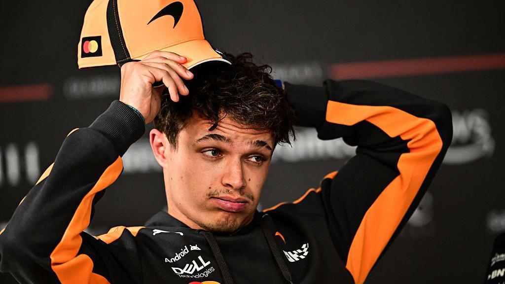 Lando Norris holds his cap above his head in the news conference in Bahrain