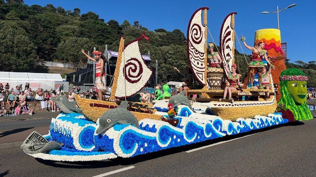 A floral float with scenes from Moana including boats and dolphins jumping out of waves.