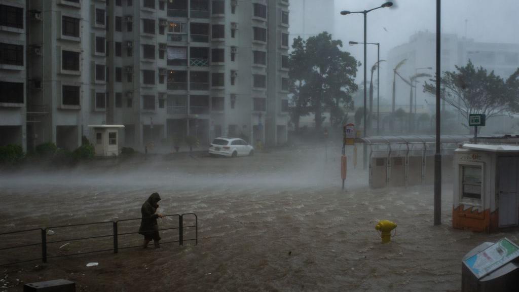 Person walking in strong winds through a flooded street in Hong Kong with tall buildings in the background
