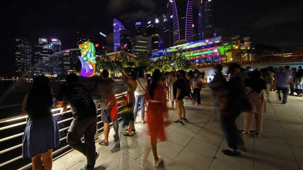 People watch light projection with illuminated artworks on the facade of the Merlion and the Fullerton Hotel at Marina Bay on 30 December 2020 in Singapore.