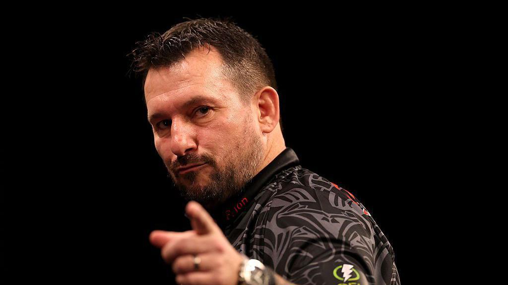 Jonny Clayton points with the index finger of his left hand as he celebrates at a Premier League darts event
