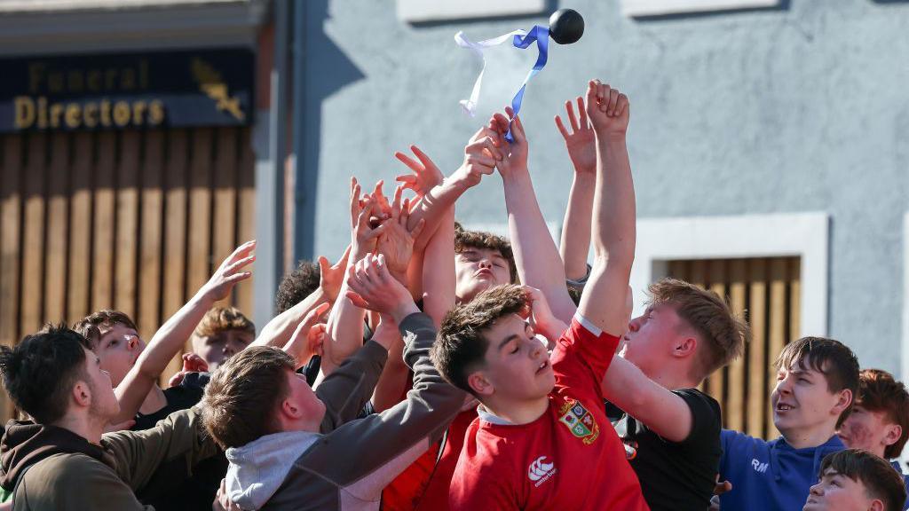 A group of young men leap to try to gather a small leather ball with a ribbon attached in Jedburgh town centre