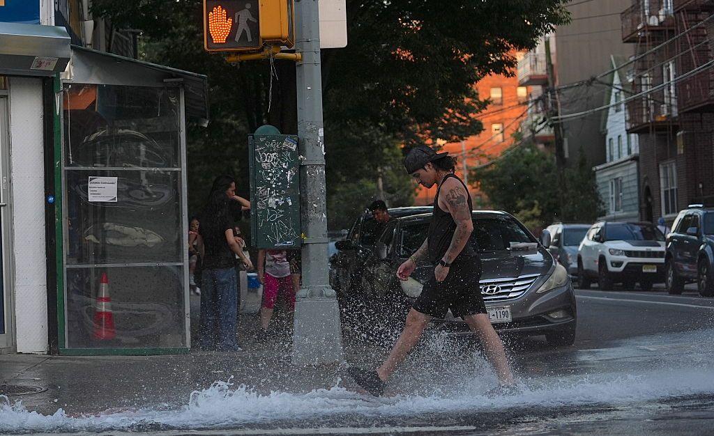 Some residents in Queens open a fire hydrant to spray cool water on their streets during extreme heat as the temperatures hit 99F (37C) in Manhattan.