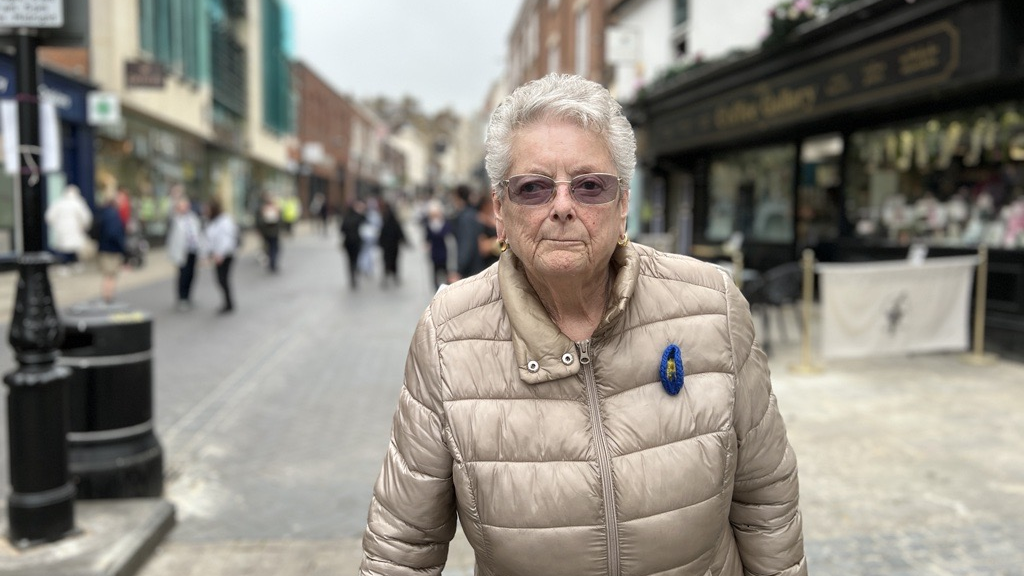 Ella Wenborne, a white woman with short, white hair, and glasses and a cream coat 