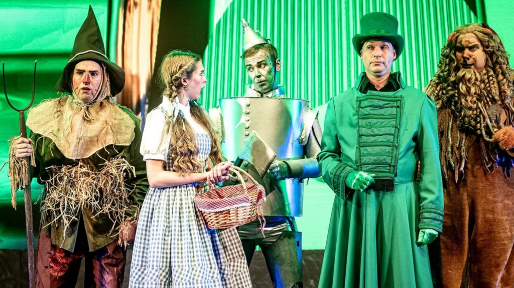 Five actors are standing on stage dressed in costume. They are characters from the Wizard of Oz.