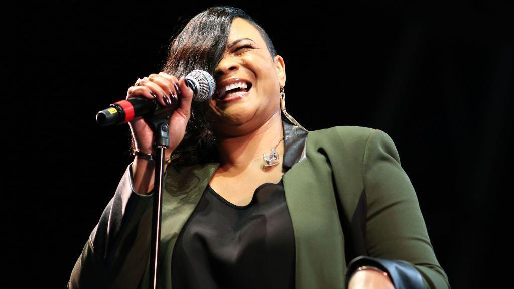 Gabrielle performs on stage wearing a green jacket and holding a microphone during Weyfest Festival 2019 