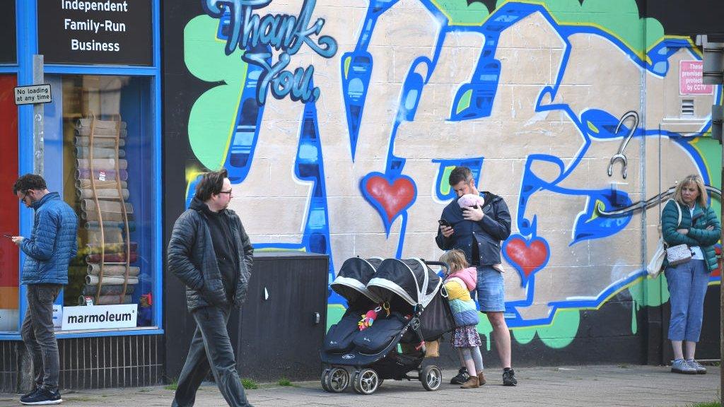 people waiting by NHS wall art