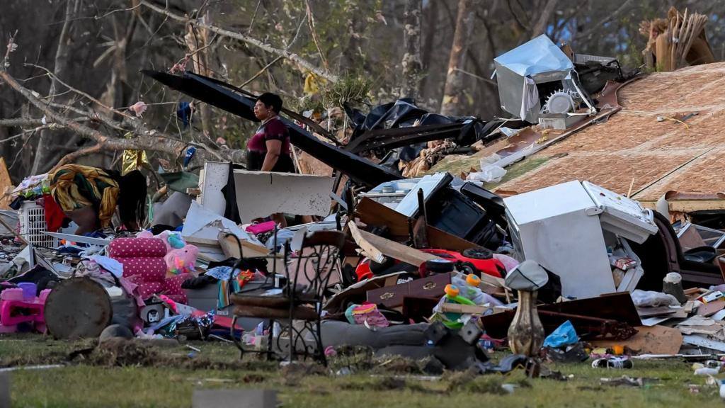 A woman walks by a destroyed home the day after a tornado in the small rural community of Wren, Mississippi