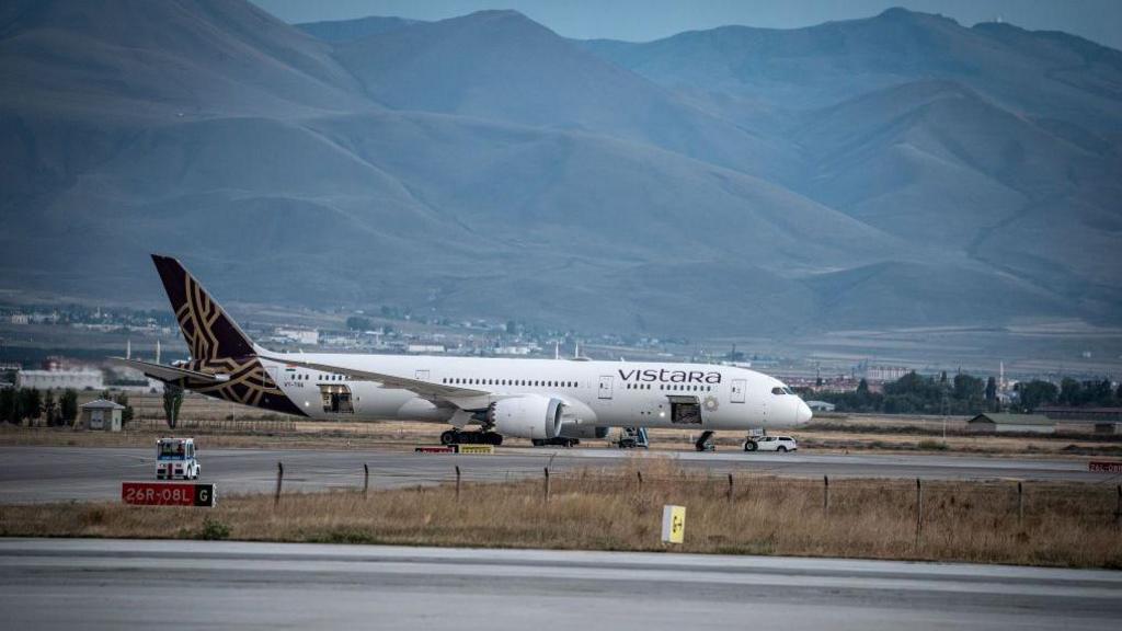 A Vistara Airlines passenger plane sits at the airport There are mountains in the background