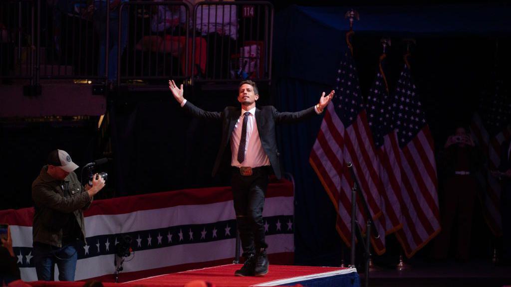 Tony Hinchcliffe striding onto stage at Madison Square Garden with his arms outstretched