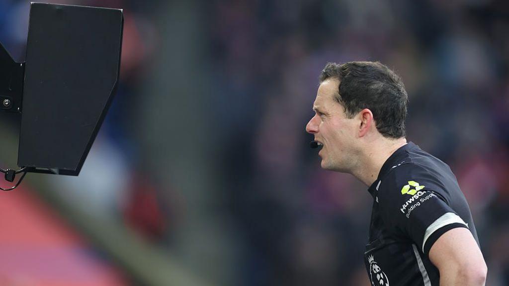 Referee Darren England leans forward to watch a replay on a pitchside monitor
