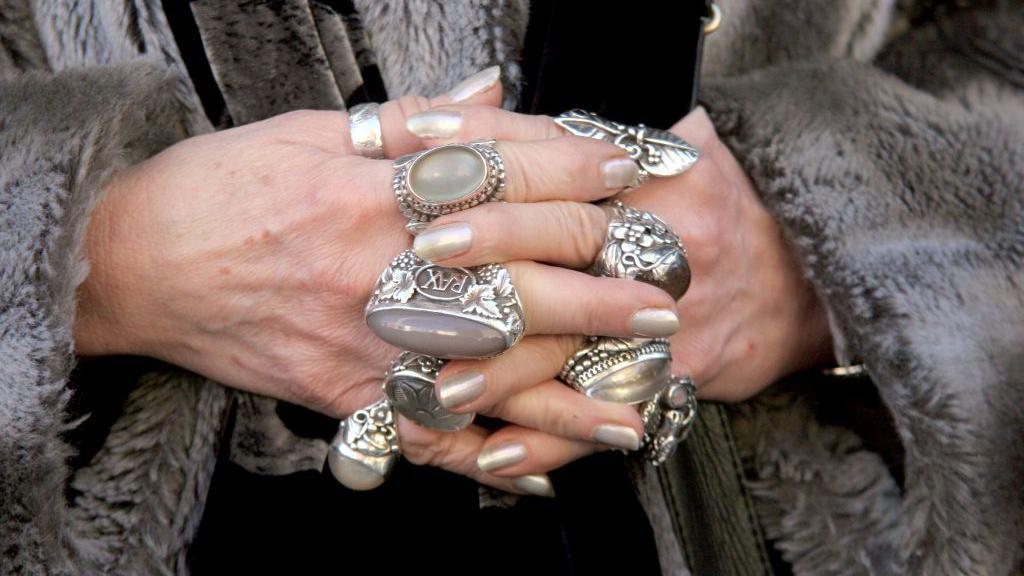 a picture of Jacqueline Wilson's clasped hands with lots of silver rings on them