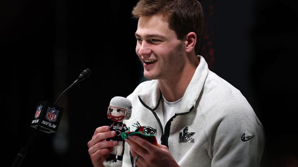 Drake Maye holding a knitted figure of himself at Super Bowl Opening Night in 2026