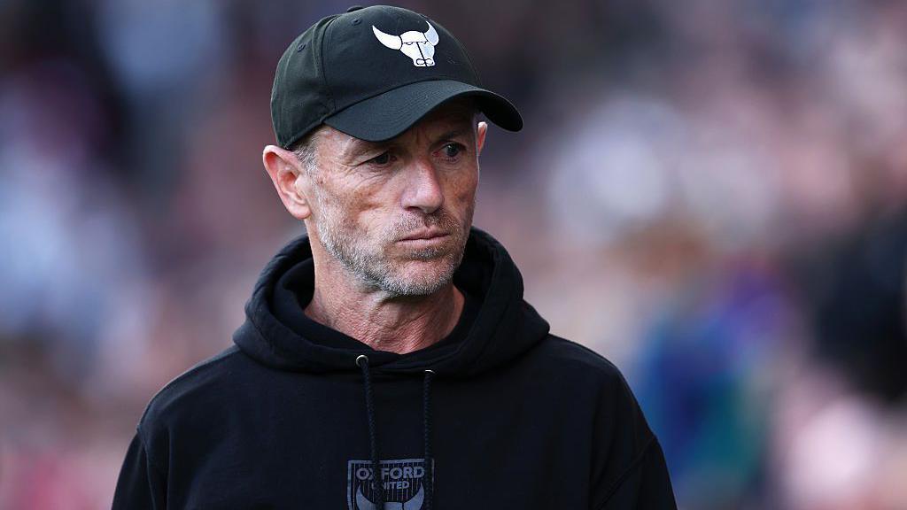 Oxford United manager Gary Rowett wearing baseball cap with Oxford bull insignia and black hoodie