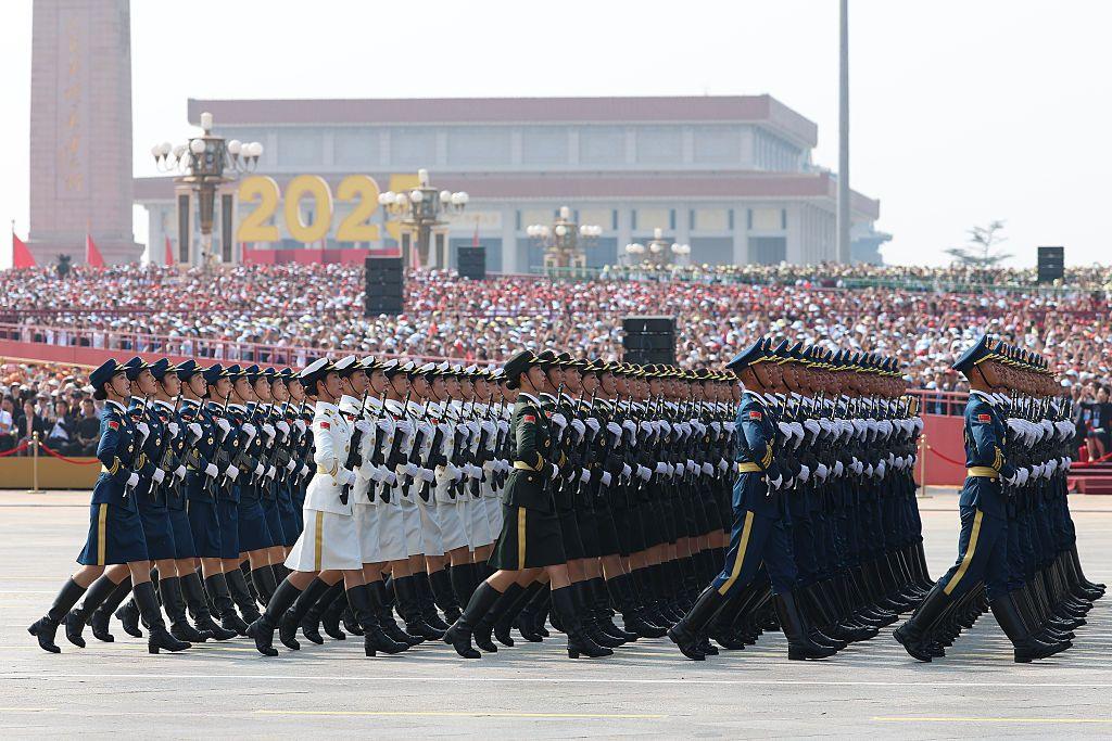 Soldiers in ceremonial uniform march in front of a crowded podium