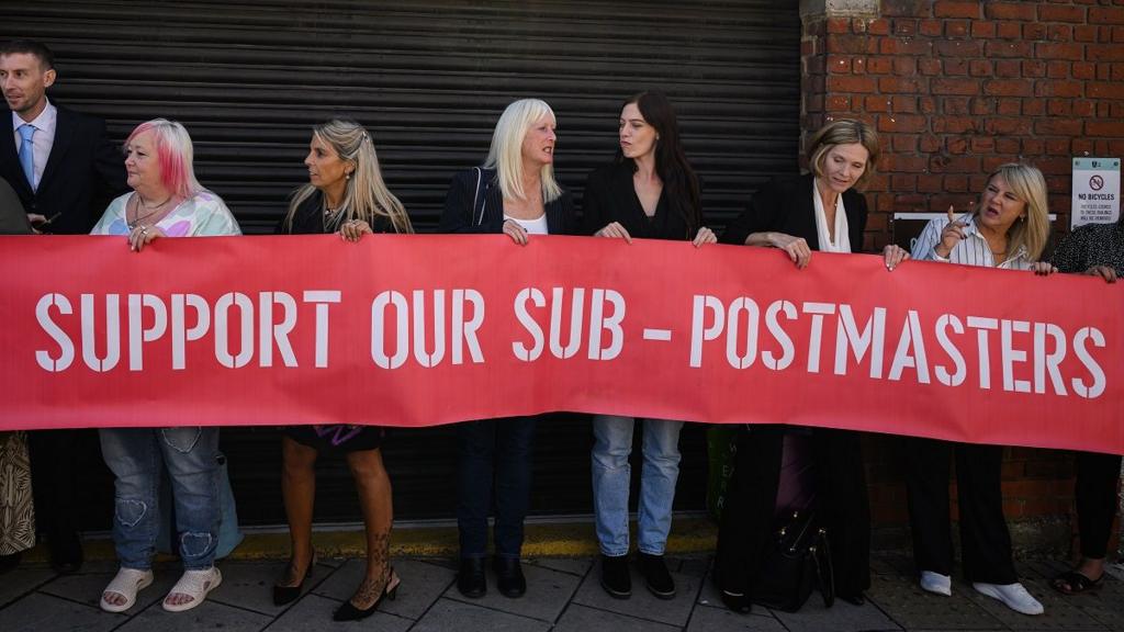 People stand with a banner reading 'support our sub-postmasters'