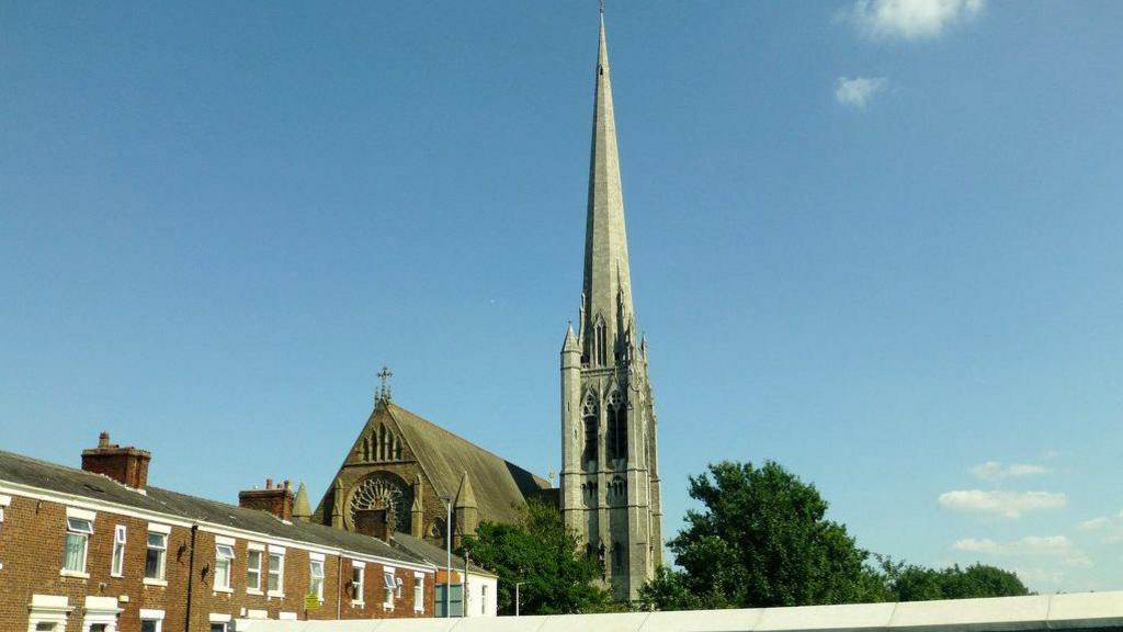 A street view of Church of St. Walburge, Preston on a sunny day close to a row of terraced homes. 