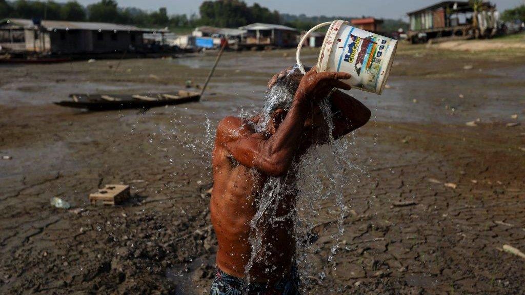 Man pouring bucket of water over himself in dried up river