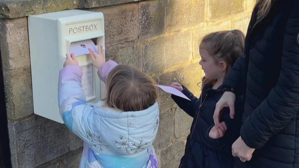 Bella (left) and Daisy (right) posting their pictures into the white "letters to heaven" post-box.