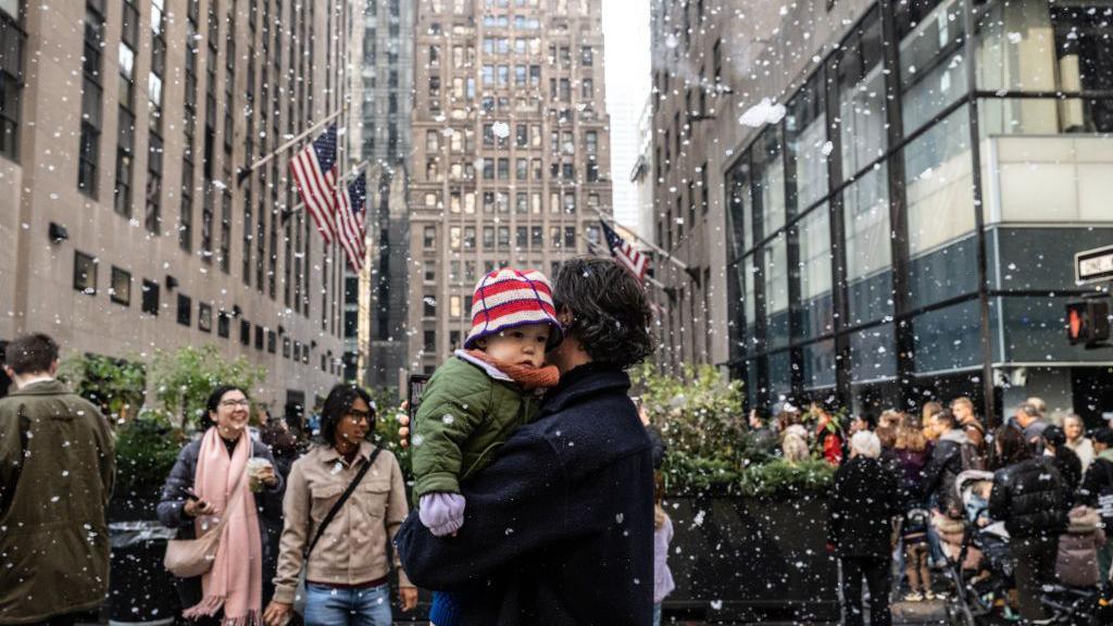 Spectators watch are covered in fake snow as the Rockefeller Center Christmas tree is installed 