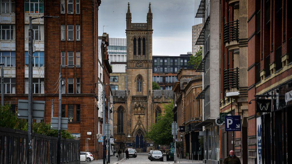 A view of a Glasgow street, with several buildings and parked cars.
