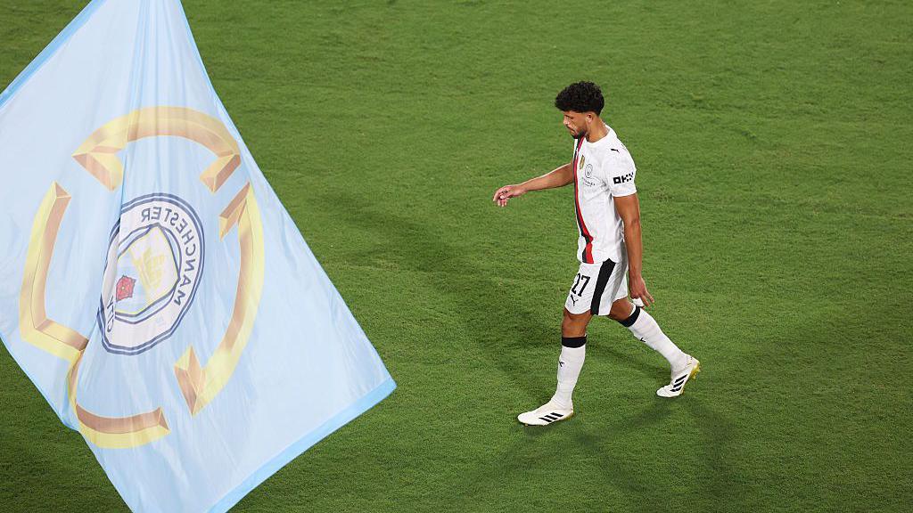 Matheus Nunes looks dejected as he walks off the pitch, with a Manchester City flag in the foreground