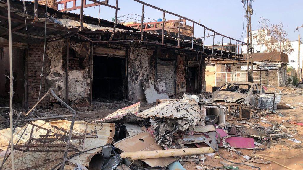 Heavily damaged shops in Omdurman, which are totally burnt out, piles of damaged debris out the front and also a burnt out car on May 30, 2024.