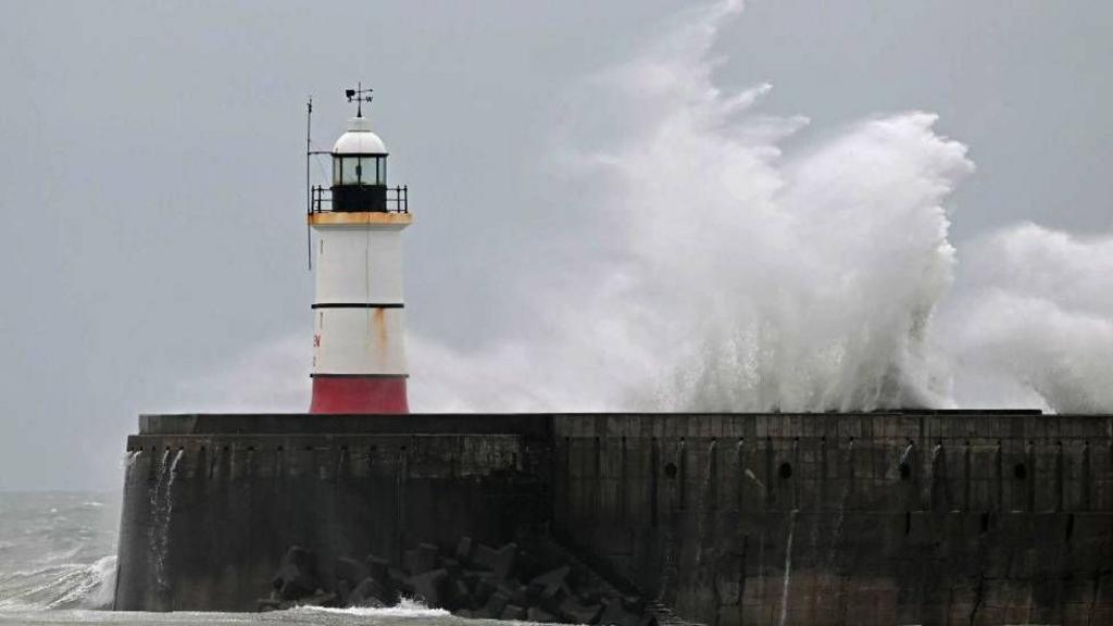 Waves crash over Newhaven Lighthouse and the breakwater in Newhaven, southern England on December 31, 2024