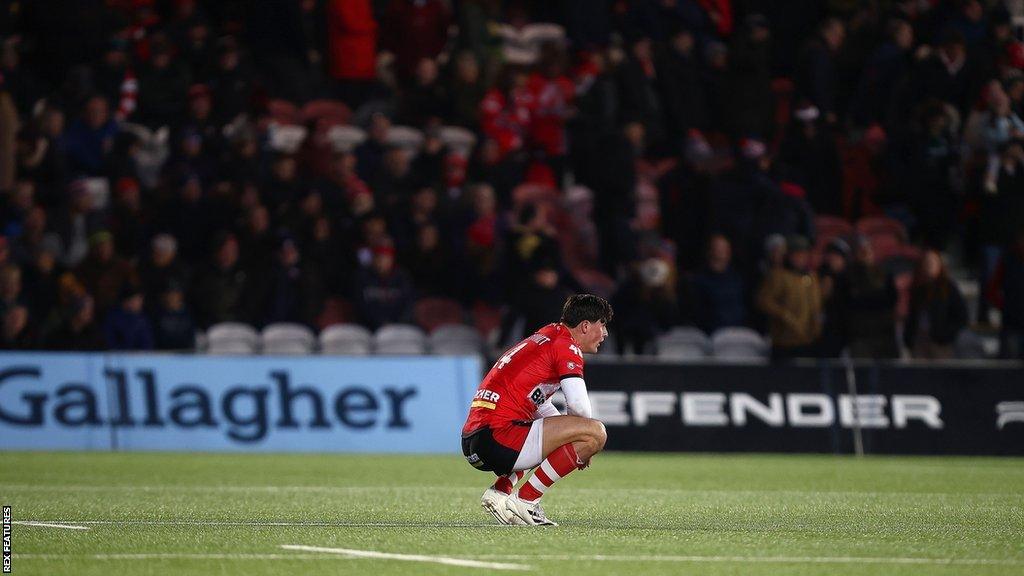 Louis Rees-Zammit kneels on the pitch alone at Kingsholm