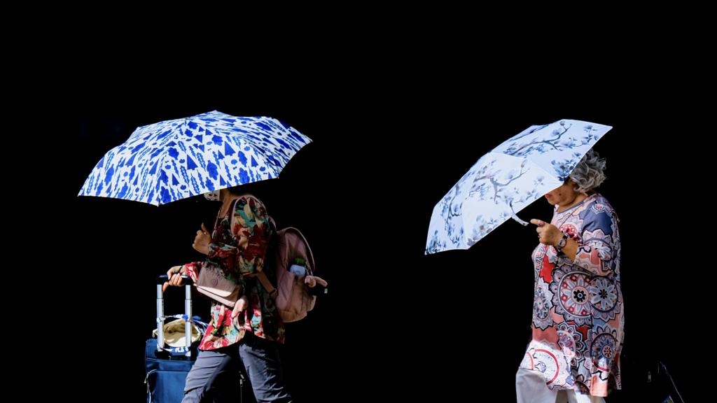 People walk with umbrellas protecting from the sun during a heat wave in Hong Kong