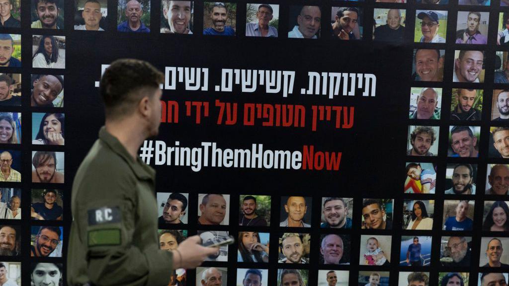 An Israeli soldier passes by a wall covered with photos of hostages held by Hamas in Gaza, at Tel Aviv train station, Israel (14 January 2025)