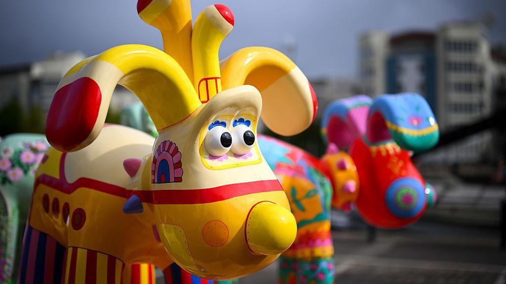 A colourfully decorated statue of Gromit from Wallace and Gromit. This one is painted yellow striped legs of different colours.
