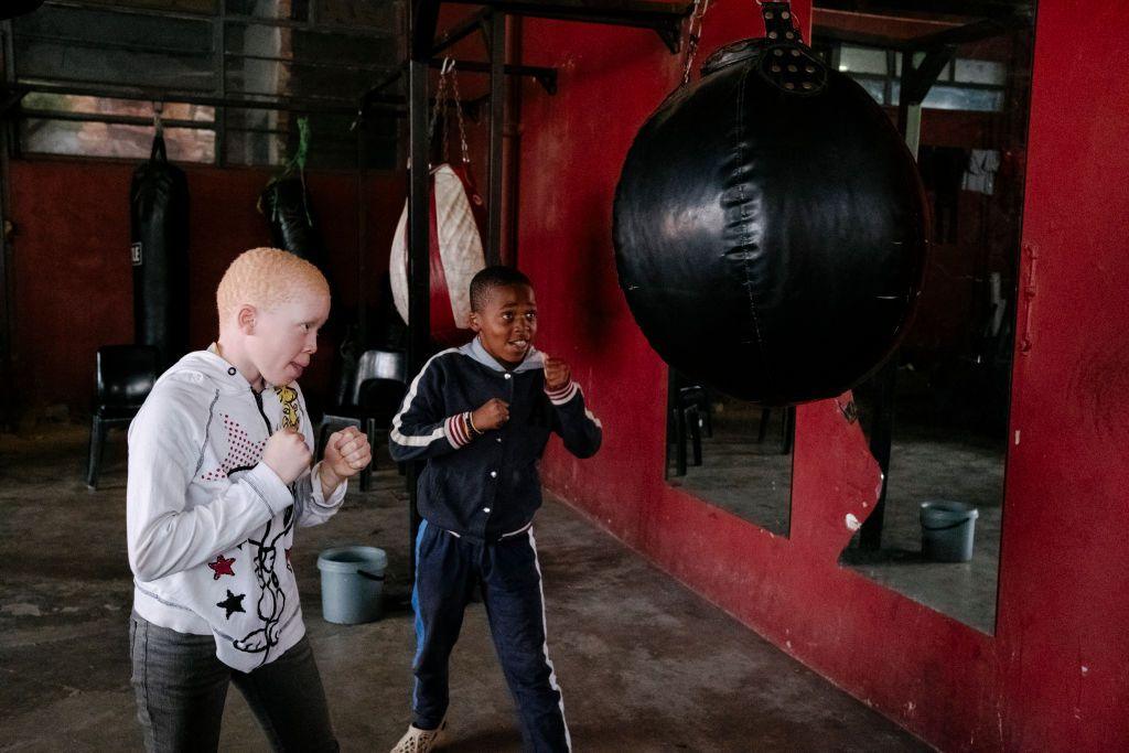 Two boys line up to punch a punch bag in a boxing gym.
