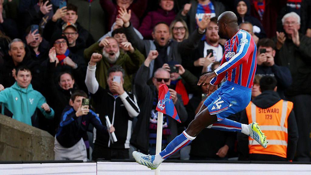 Jean-Philippe Mateta leaps near the corner flag as he celebrates scoring for Crystal Palace against Newcastle United, with fans celebrating in the stands
