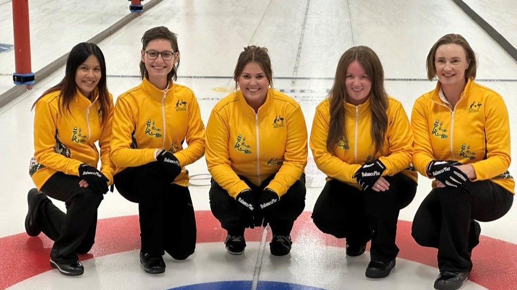 A line-up of women in yellow Australia tops on a curling rink