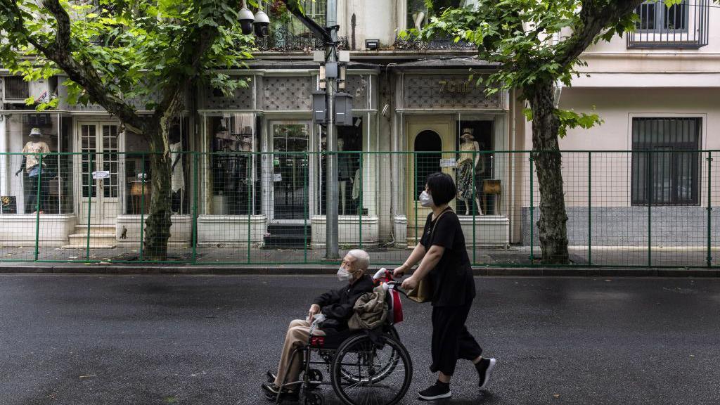 A woman wheels a man in a wheelchair past a fence surrounding a neighborhood placed under lockdown due to Covid-19 in Shanghai, China, on Friday, June 10, 2022. 