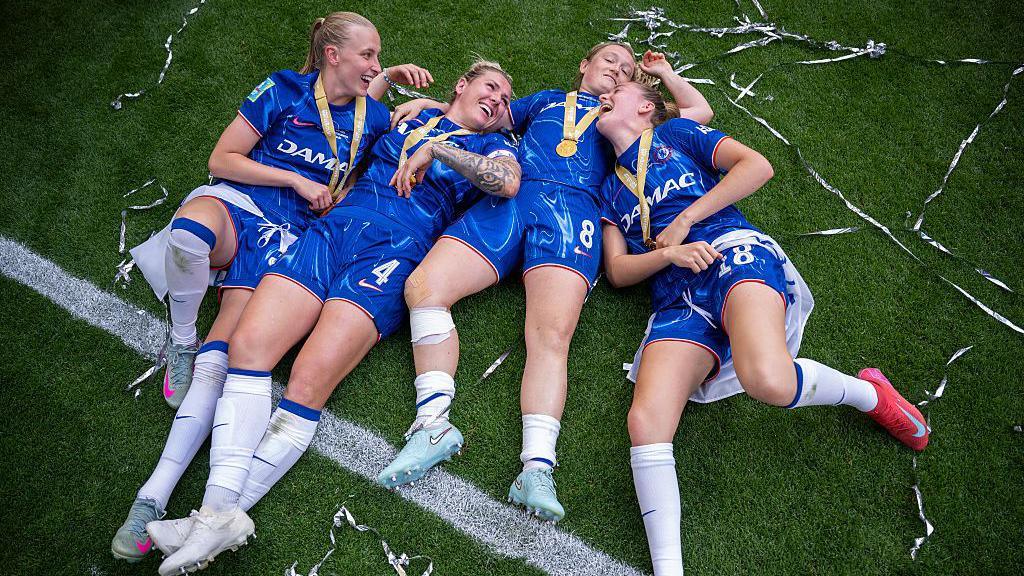 Agnes Beever-Jones, Millie Bright, Erin Cuthbert and Wieke Kaptein lying on the pitch celebrating their victory.