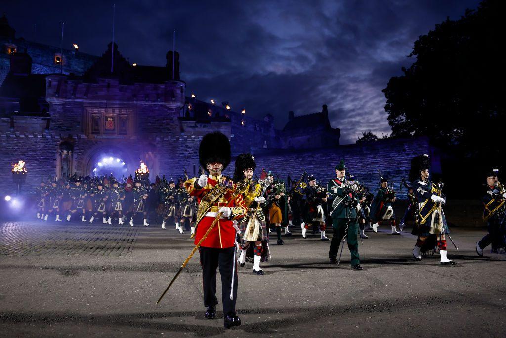 A military band marches and plays in front of Edinburgh Castle at night during the Military Tattoo