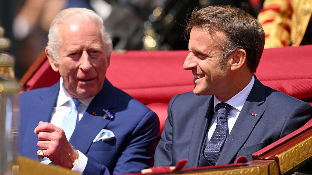 King Charles and French President Emmanuel Macron talk animatedly to each other as they travel through Windsor in an open-topped carriage on 8 July 2025