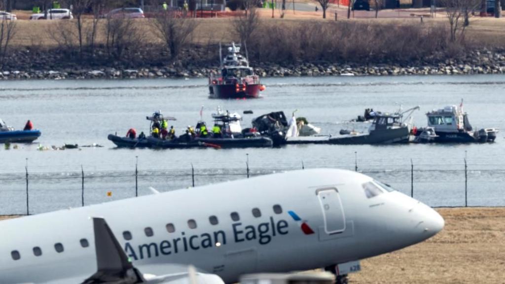 A plane with "American Eagle" written on its body, with ships on the river behind appearing to carry wreckage