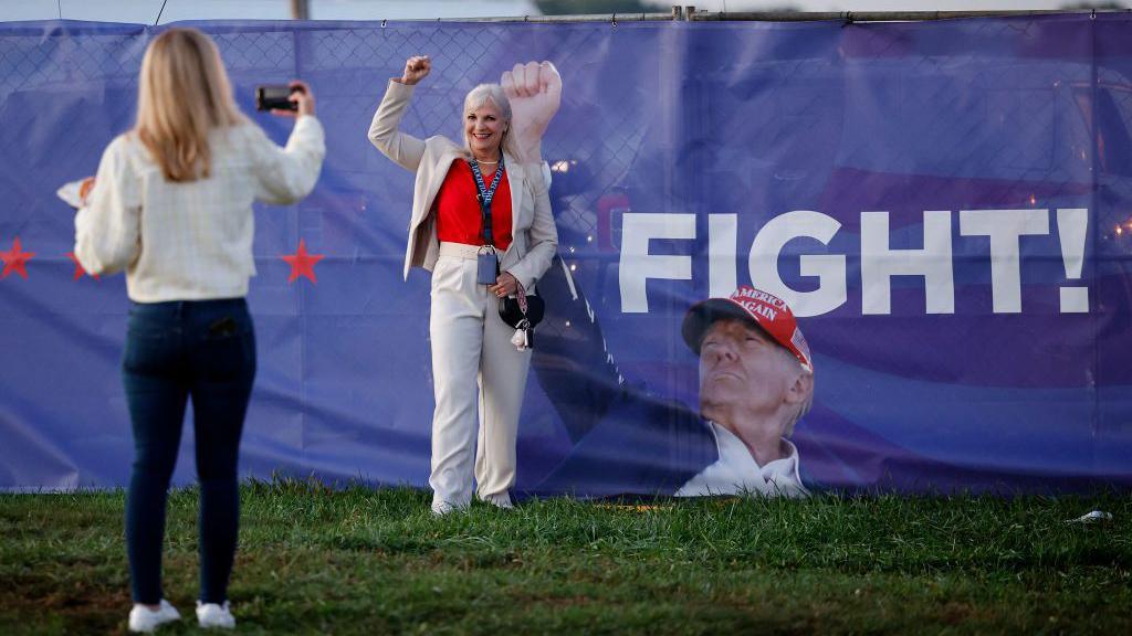 A woman takes a photo in front of a picture of Republican presidential nominee, former US President Donald Trump, prior to a rally at the Butler Farm Show Inc. on October 05, 2024 in Butler, Pennsylvania