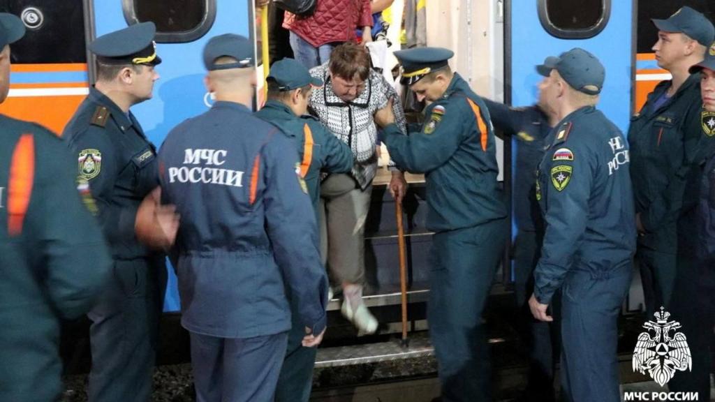 Officials help a resident of Kursk off a train as part of evacuation efforts