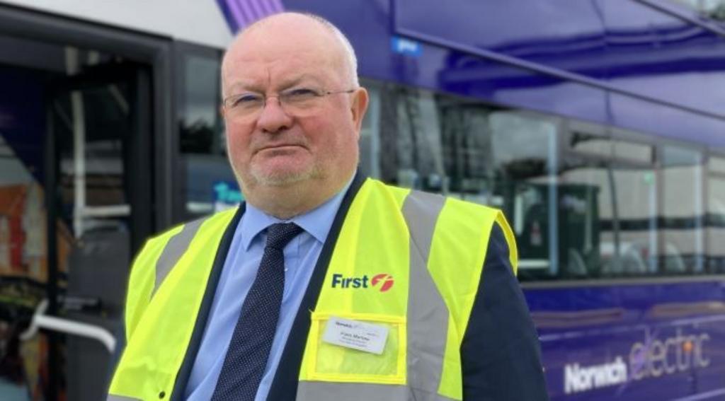 Piers Marlow standing in front of a First Bus bus with the words "Norwich electric" visible on its side