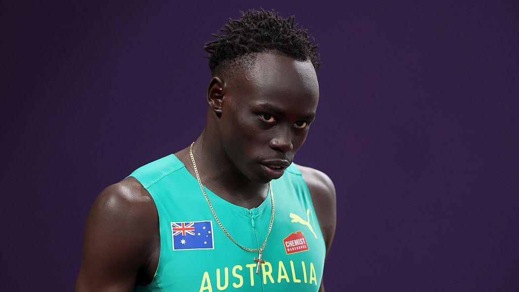 Gout Gout wears green Australia running gear and faces forwards with a purple background behind.