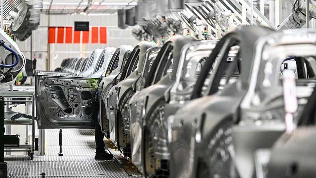 A worker inspects an electric car at a Zeekr factory in Meishan Island in Ningbo, in China's eastern Zhejiang Province on April 18, 2025. The photo shows a row of silver-coloured vehicles at a factory.  