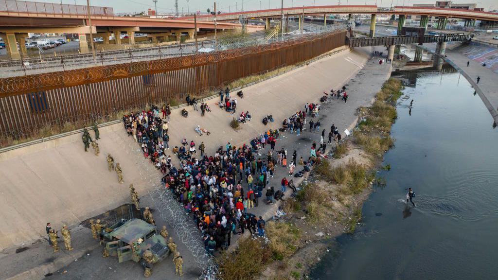 Texas officials stand near razor wire as migrants cross water