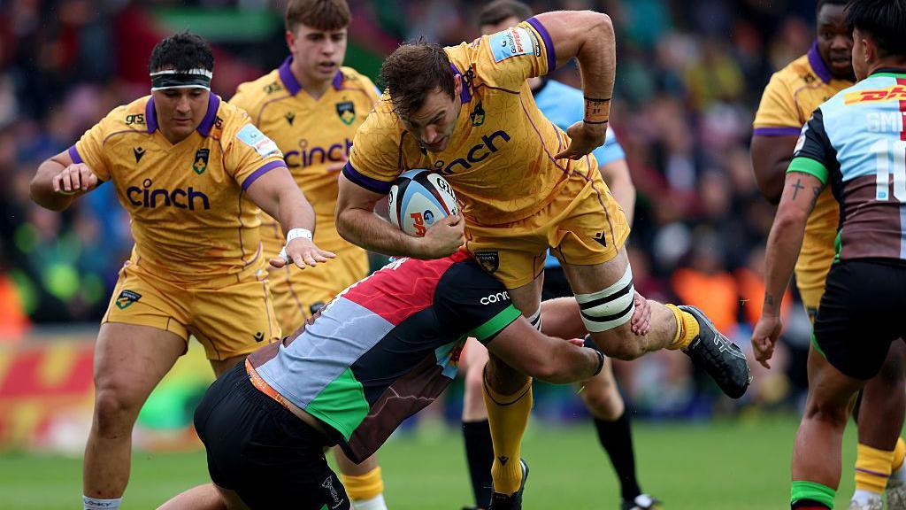 Northampton back row Josh Kemeny drives through a Harlequins tackle at The Stoop