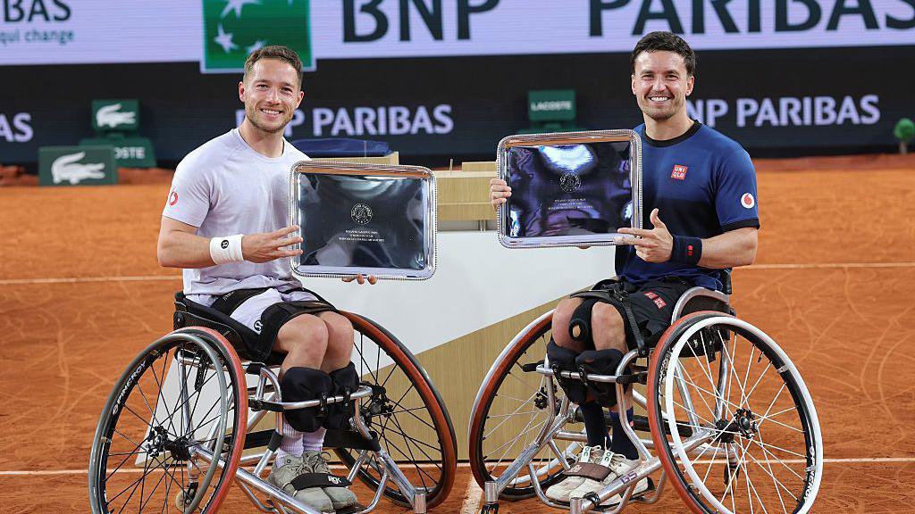 Alfie Hewett and Gordon Reid hold up their French Open men's wheelchair doubles trophies in 2025