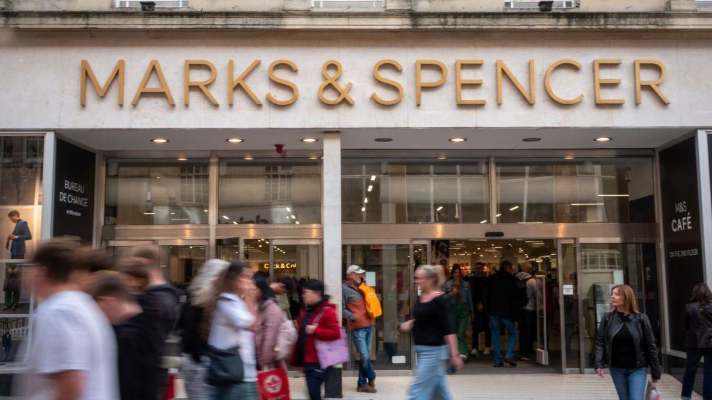 An M&S store front with shoppers walking past
